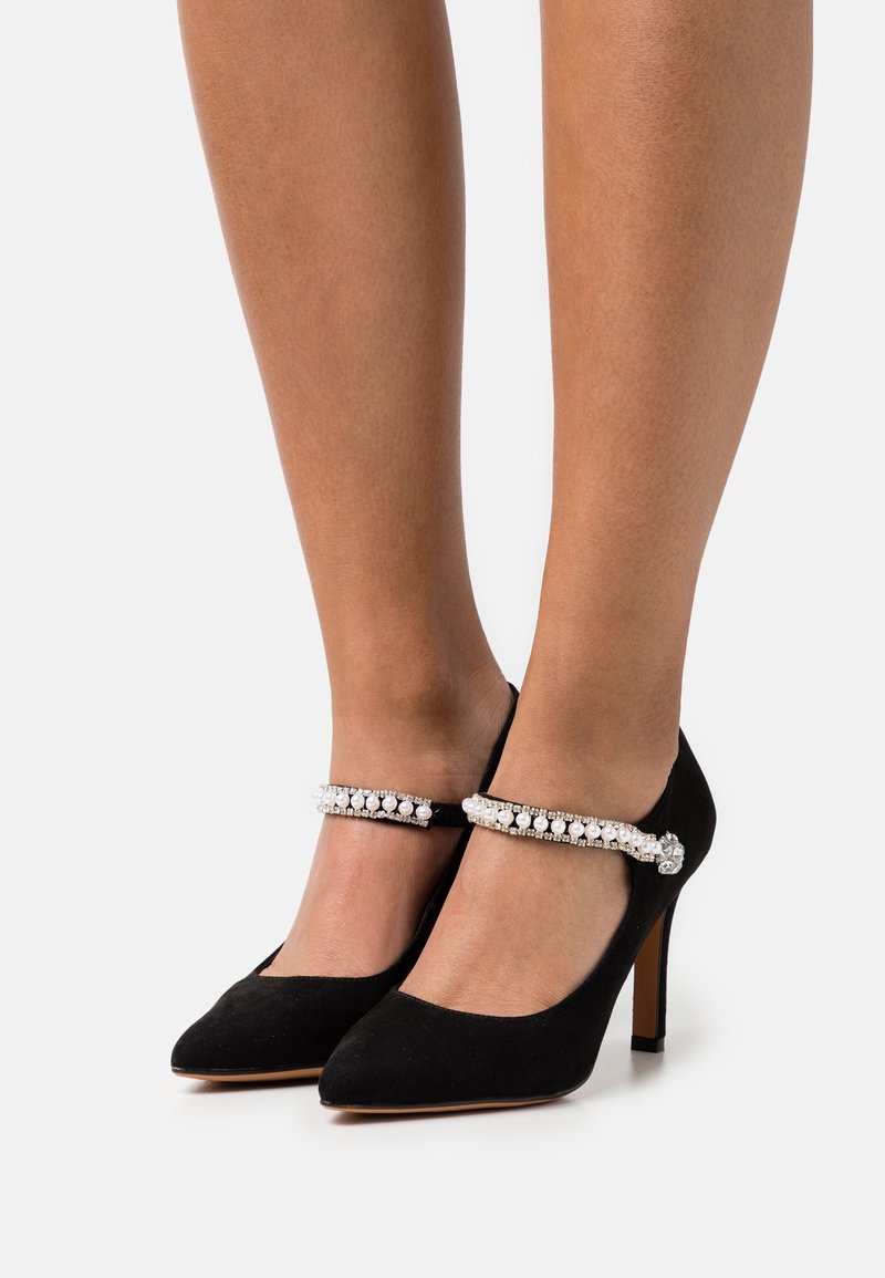 Chaussures à talons hauts en suede noir avec bout pointu et bride de cheville ornée d'une rangée de perles blanches et de rhinestones.