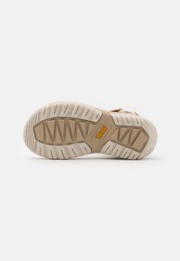 Light beige sandal sole with textured traction patterns, featuring a patterned rubber base and a raised logo in orange color.