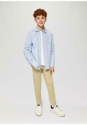 Helles blau gestreiftes Hemd über einem weißen T-Shirt, kombiniert mit beigen Hosen und weißen Sneakers mit dunkelblauen Akzenten.