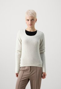 Gaiši pelēks džemperis, kas izgatavots no mīksta materiāla, ar apaļu kakla izgriezumu, garām piedurknēm un ribota aproces dizainu. Saskaņots ar brūniem biksēm.