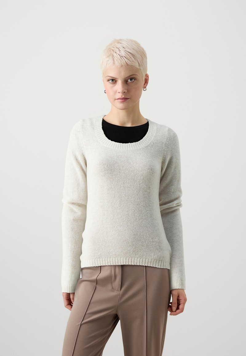 Gaiši pelēks džemperis, kas izgatavots no mīksta materiāla, ar apaļu kakla izgriezumu, garām piedurknēm un ribota aproces dizainu. Saskaņots ar brūniem biksēm.