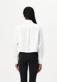 Hvit, kortermet skjorte med lange ermer, knapplukking og en ryggfold; sammen med svarte, tettsittende bukser. Glatt tekstur, minimalistisk design.