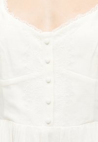 Λευκό μπούστο φορέματος με κουμπιά καλυμμένα με ύφασμα στο κέντρο και λεπτή δαντέλα κατά μήκος του V-λαιμού.