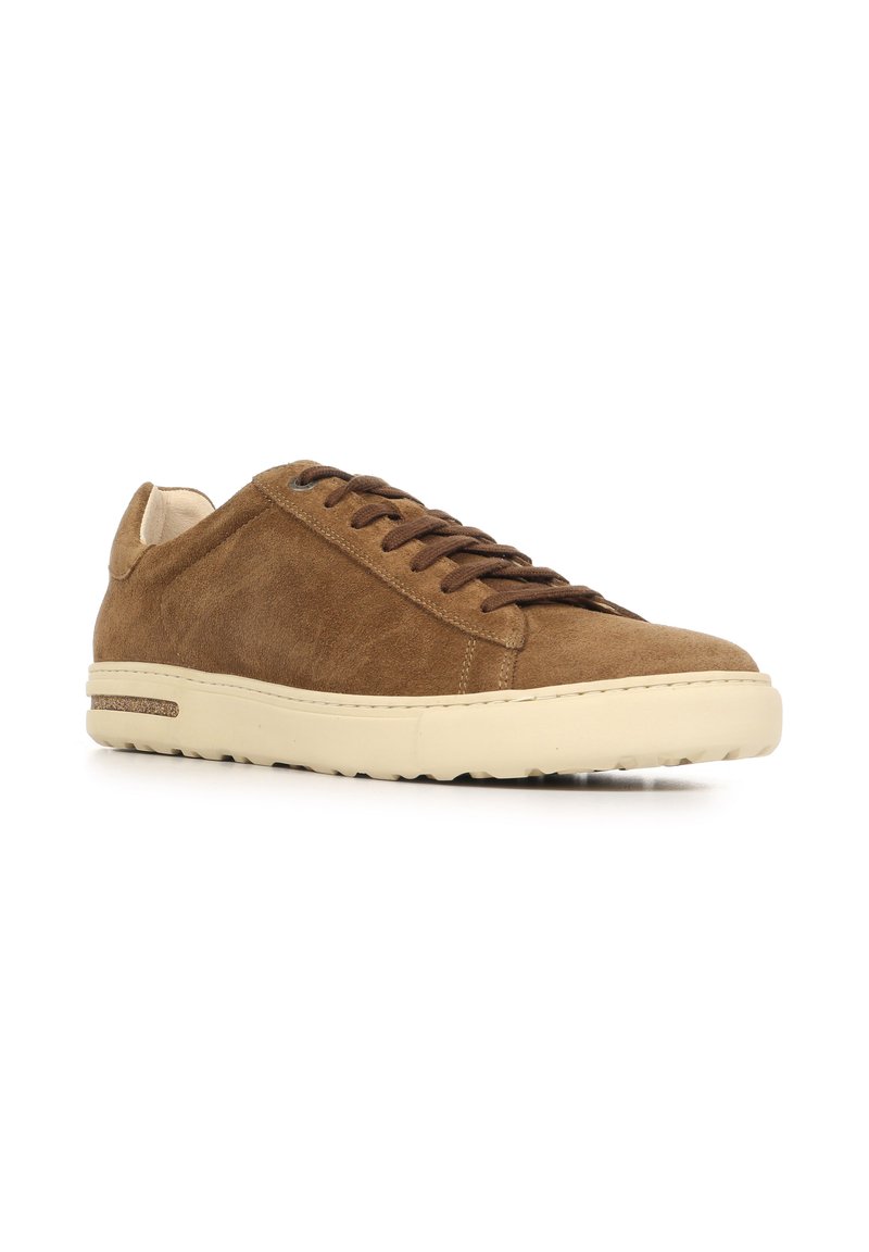 Brown suede sneaker with a low profile, round toe, and cream-colored rubber sole. Features thin laces and minimal stitching details.
