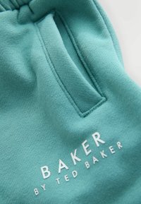 Tyrkysové bavlněné tepláky s boční kapsou a potiskem loga „BAKER BY TED BAKER“ v bílé barvě na spodní části přední strany. Hladká textura.