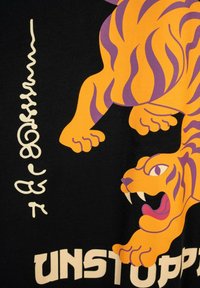 Pomarańczowo-fioletowy tygrys z otwartą paszczą i ostrymi zębami na czarnym tle, z stylizowanym pionowym napisem i częściowym słowem "UNSTOPP" poniżej.