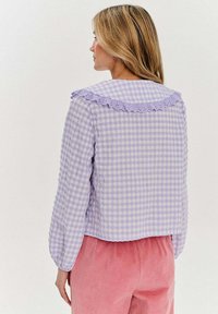 Fioletowa i biała koszula w kratę z koronkową krawędzią w kształcie fali, długimi rękawami i luźnym krojem, zestawiona z różowymi spodniami z sztruksu.