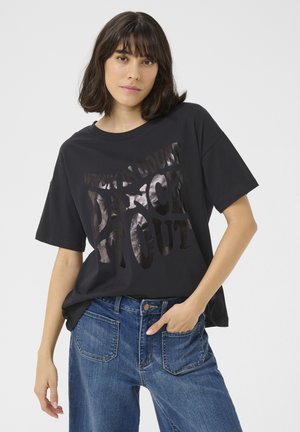 Black short-sleeve t-shirt with shiny silver text saying "WHEN IN DOUBT DANCE IT OUT." Relaxed fit, made from soft fabric. Paired with blue jeans.