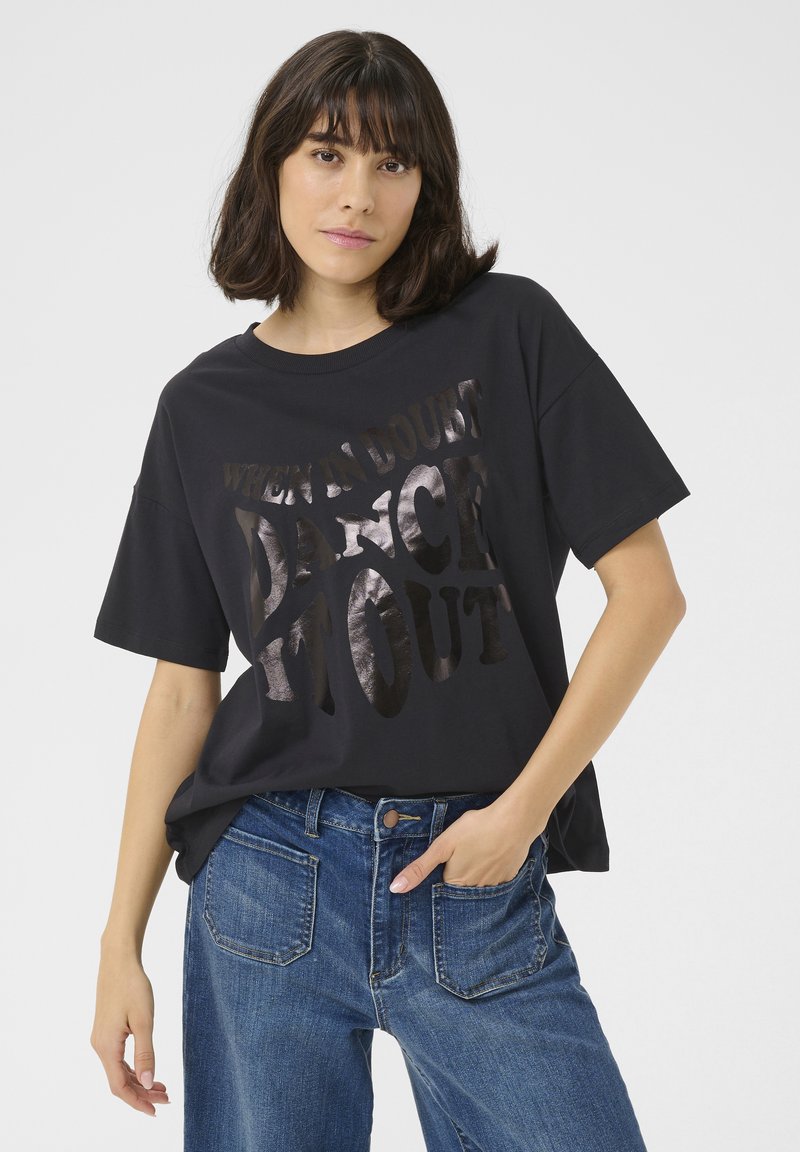 Schwarzes T-Shirt mit kurzen Ärmeln und glänzendem silbernen Text, der sagt: "WENN ZWEIFEL HERRSCHT, TANZE DAVON." Lässiger Schnitt, aus weichem Stoff gefertigt. Kombiniert mit blauen Jeans.
