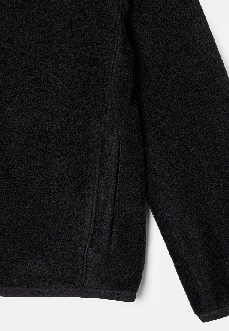 Schwarze Fleecejacke mit einer weichen, strukturierten Oberfläche, ausgestattet mit einer Seitentasche und einem abgerundeten Saum. Das Design ist einfach und funktional.
