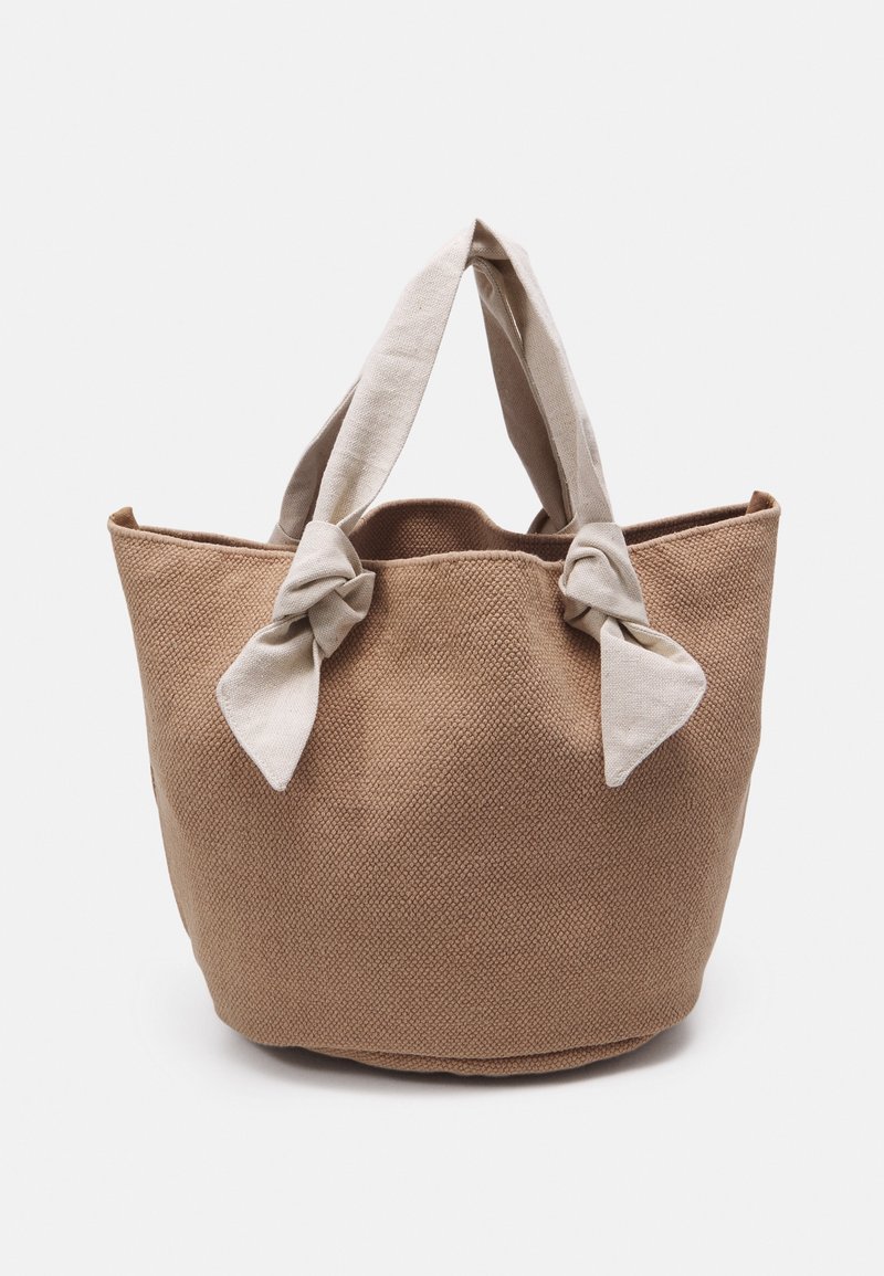 Sac fourre-tout tissé brun à la surface texturée, avec deux anses en tissu clair nouées en nœud sur le dessus.