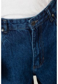 Denim jeans in dark blue with a textured finish. Features a metal button closure, belt loops, and contrasting orange stitching details.