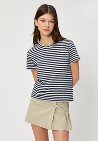 T-shirt in cotone a righe blu navy e bianche, maniche corte, scollo rotondo, vestibilità comoda; abbinato a una gonna beige con dettaglio cinturino laterale.