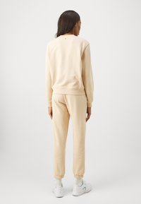 Beige sweatshirt en joggers set, met een zachte textuur, geribde manchetten en een klein accentdetail op de achterkant van de sweatshirt.