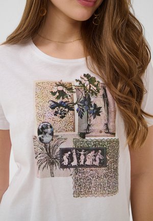 Femme portant un T-shirt blanc avec des impressions mixtes de style vintage, incluant des fleurs, un palmier, des figures classiques et des motifs ornementaux.