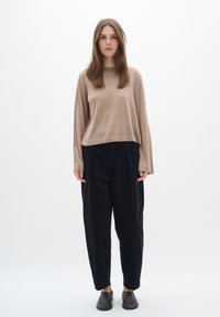Pullover marrone chiaro, strutturato, con maniche lunghe, abbinato a pantaloni neri dalla vestibilità ampia. Scarpe slip-on nere completano il look.
