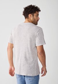 Maglione grigio chiaro a maniche corte con un design a maglia testurizzata, caratterizzato da un collo rotondo e una vestibilità rilassata, abbinato a jeans blu chiaro.