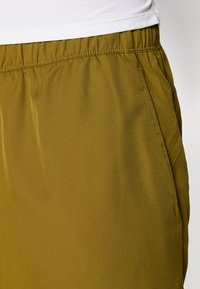 Khakifarbene Shorts mit elastischem Bund, aus einem glatten, leichten Stoff gefertigt. Verfügt über Seitentaschen und eine leichte Schimmerung in der Textur.