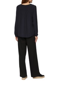 Marineblauwe blouse met lange mouwen, een losse pasvorm, geweven stof en een geplooide achterkant. Gecombineerd met zwarte wijde broek en zwarte sneakers.