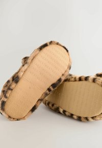 Pantofle z umělé kožešiny s leopardím vzorem, s béžovou stélkou, mají texturovanou podrážku s raženým logem značky a zaoblený tvar.