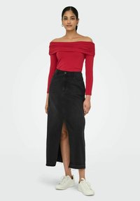 Czerwona bluzka typu off-shoulder z marszczonym wzorem, zestawiona z czarną dżinsową maksispódnicy z rozcięciem z przodu i postrzępionym dołem, noszona z białymi sneakersami.