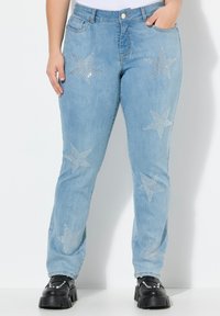 Jeans de mezclilla azul claro con adornos de estrellas plateadas en la parte delantera. Tienen un diseño de pierna recta y se combinan con zapatos negros gruesos.