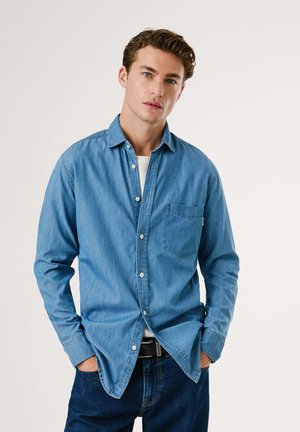 Lichtblauwe denim knoopshirt met een borstzak, kraag, lange mouwen en een relaxte pasvorm, gecombineerd met donkere denim jeans.
