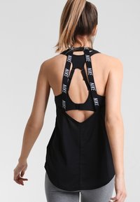 Top sportivo nero con dettaglio posteriore a taglio, dotato di spalline con marchio Nike e una vestibilità ampia, progettato per comfort e traspirabilità.