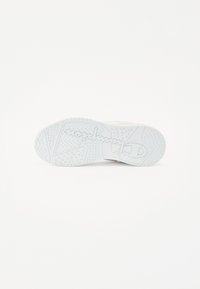 Semelle de sneaker blanche avec une surface en caoutchouc texturée présentant un motif en zigzag. Détail de logo manuscrit notable au centre.