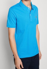 Camiseta polo azul hecha de tejido texturizado, con un cuello clásico, mangas cortas y un pequeño logo verde en el lado izquierdo del pecho.