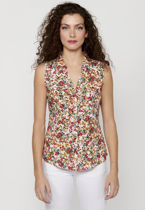 Blouse sans manches à motifs floraux avec un décolleté en V ; présente un mélange de motifs rouges, jaunes et verts sur fond blanc ; tissu léger.