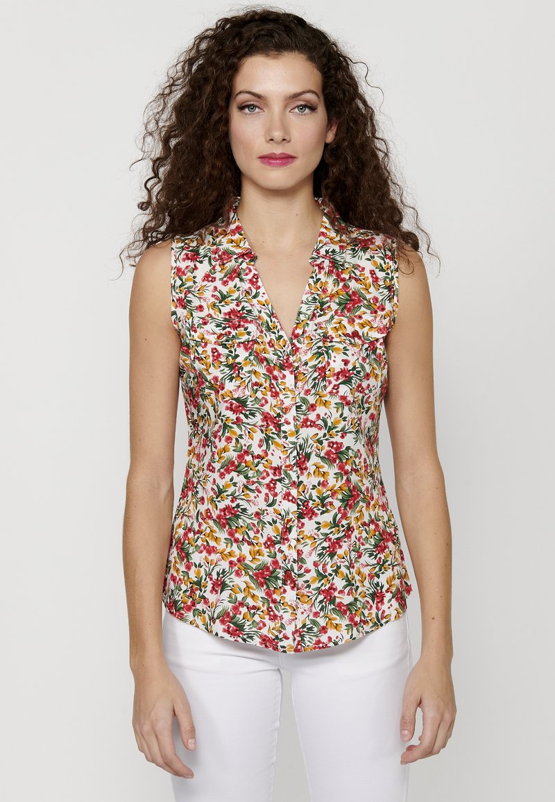 Blusa senza maniche floreale con scollatura a V; presenta un mix di motivi rossi, gialli e verdi su uno sfondo bianco; tessuto leggero.