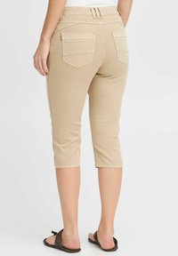 Pantaloni beige a vita corta realizzati in un tessuto elasticizzato con una texture liscia, dotati di due tasche posteriori e un design slim fit.