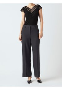 Zwarte geribbelde top met kantdetails bij de halslijn, gecombineerd met zwarte op maat gemaakte wijde broekspijpen. Puntige zwarte hakken maken de look compleet.