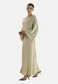 Beige jurk met lange mouwen, een vloeiende silhouet, textuurstof en brede klokmouwen. Gecombineerd met transparante hoge hakken zonder patronen.