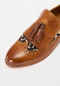 Pantof cu toc rotund din piele maro, cu accente de imprimeu leopard negru, ciucuri franjurați și perforații decorative.