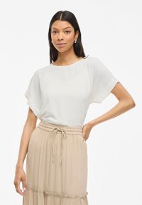 Top bianco a maniche corte con una vestibilità relaxed, abbinato a una gonna plissettata beige con elastico in vita e orlo arricciato.