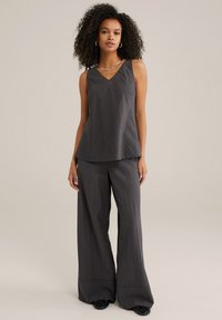 Haut sans manches gris avec un décolleté en V et un design fluide, associé à un pantalon évasé, le tout dans un tissu texturé.