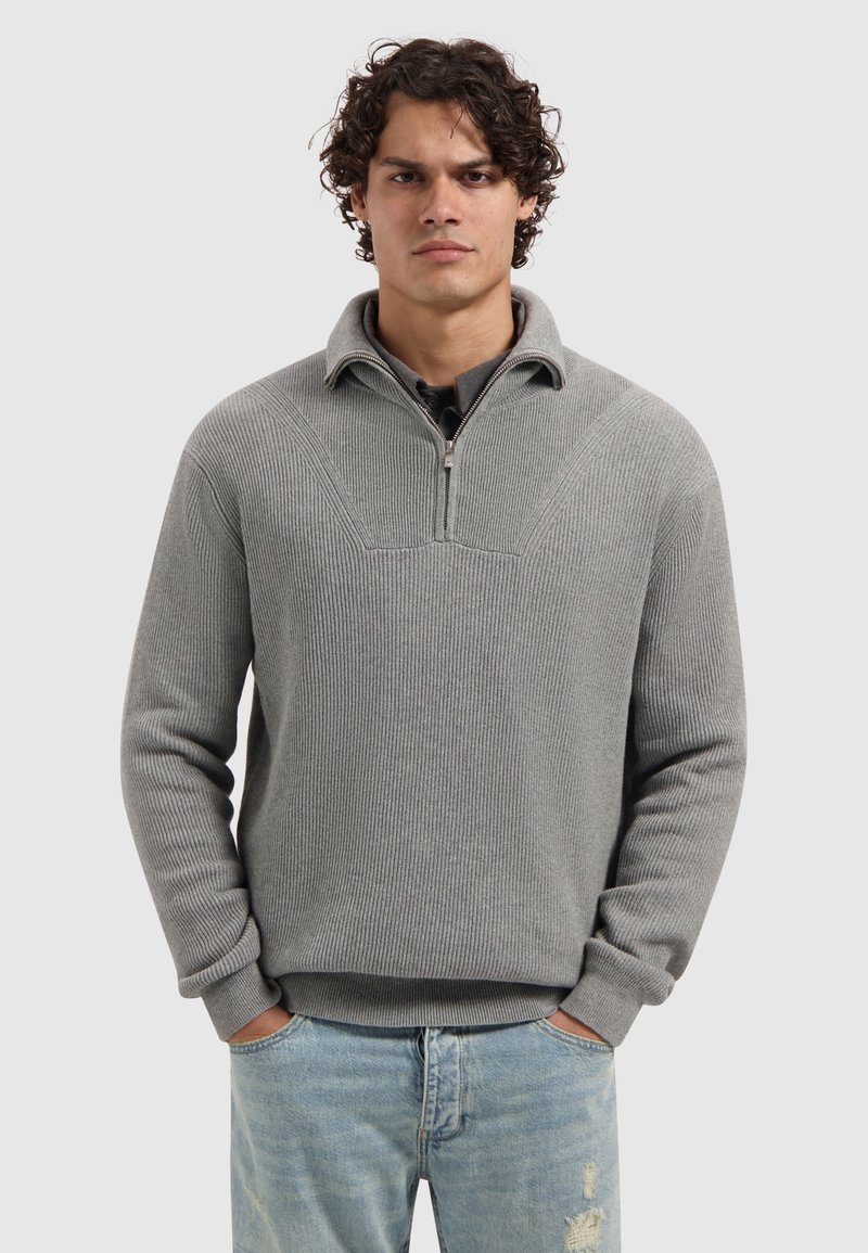Grijze gebreide pullover trui met een kwart-rits kraag en ribbeltextuur. Voorzien van lange mouwen en een relaxte pasvorm. Draag met lichtblauwe spijkerbroeken.