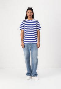Stripete t-skjorte i blått og hvitt med rund hals og en liten logo på brystet, sammen med lyseblå jeans og hvite joggesko.