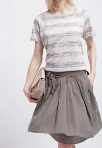 Top de manga corta a rayas en rosa y gris, combinado con una falda gris con pliegues y cintura atada. Se sostiene un bolso de mano ligero en una mano.