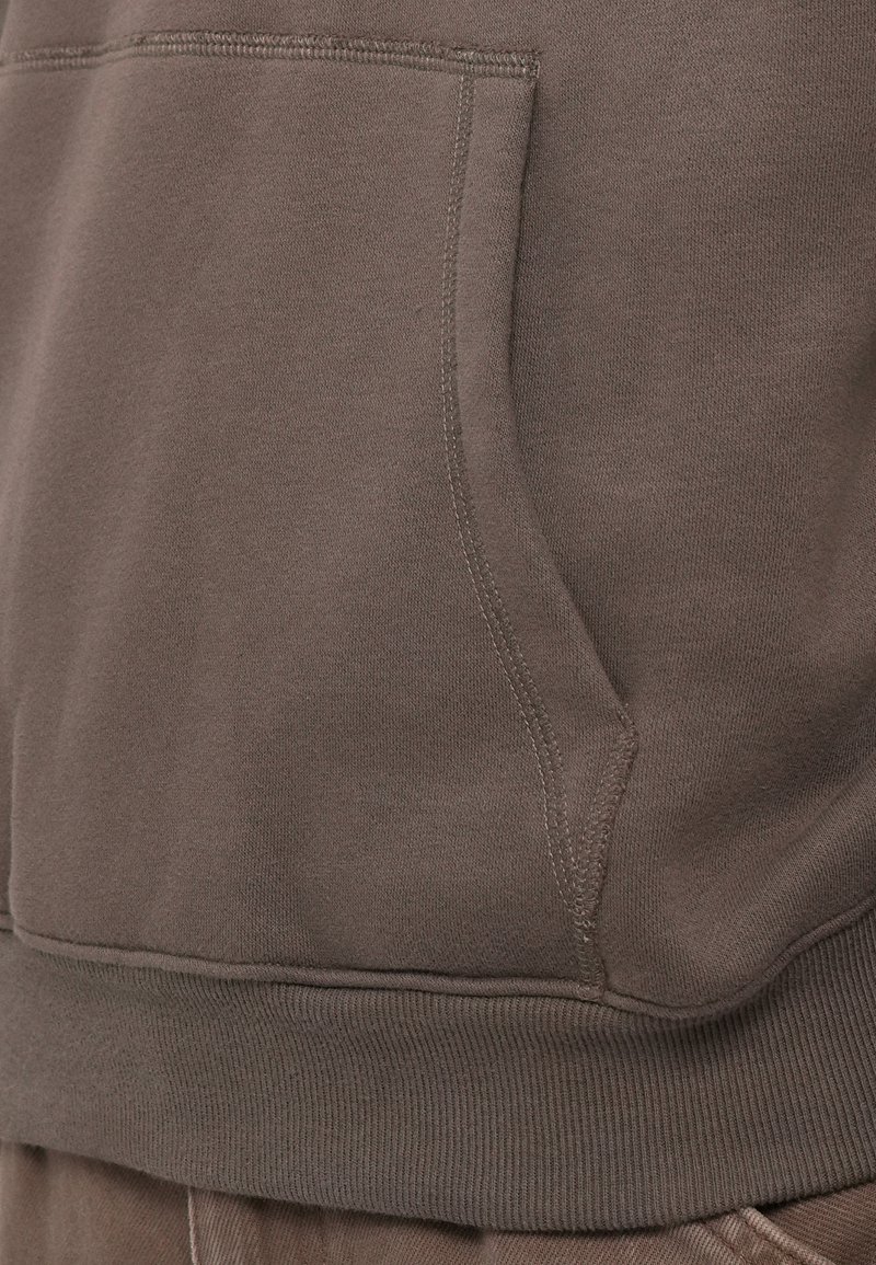 Brązowa bluza z kapturem z kieszenią z przodu, ściągaczem u dołu i na mankietach, o miękkiej fakturze i widocznych detalach szwów.