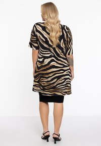 Schwarz-gepunktetes Tiermusterkleid mit kurzen Ärmeln, mid-thigh Länge und einem fließenden Design, getragen über einem schmalen schwarzen Rock und kombiniert mit Absatzschuhen.