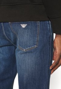 Mellanblå jeans i denim med subtil textur. Har kontrasterande sömmar och en liten vit logotyp på bakfickan.