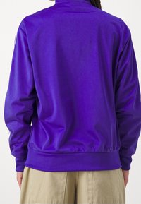 Lila träningsjacka med hög krage, tillverkad av slätt material. Har en åtsittande midja och långa ärmar. Enkel design, utan mönster.