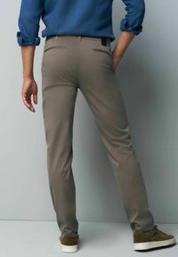 Light brown pants with a slim fit, featuring a smooth texture, back pockets, and a subtle logo tag, paired with dark green sneakers.
