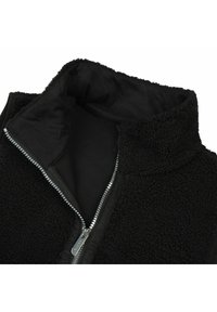 Schwarze Fleece-Weste mit hohem Kragen, ausgestattet mit einem metallischen Reißverschluss und weicher Innenausstattung. Strukturierte Außenseite für Wärme und Komfort.