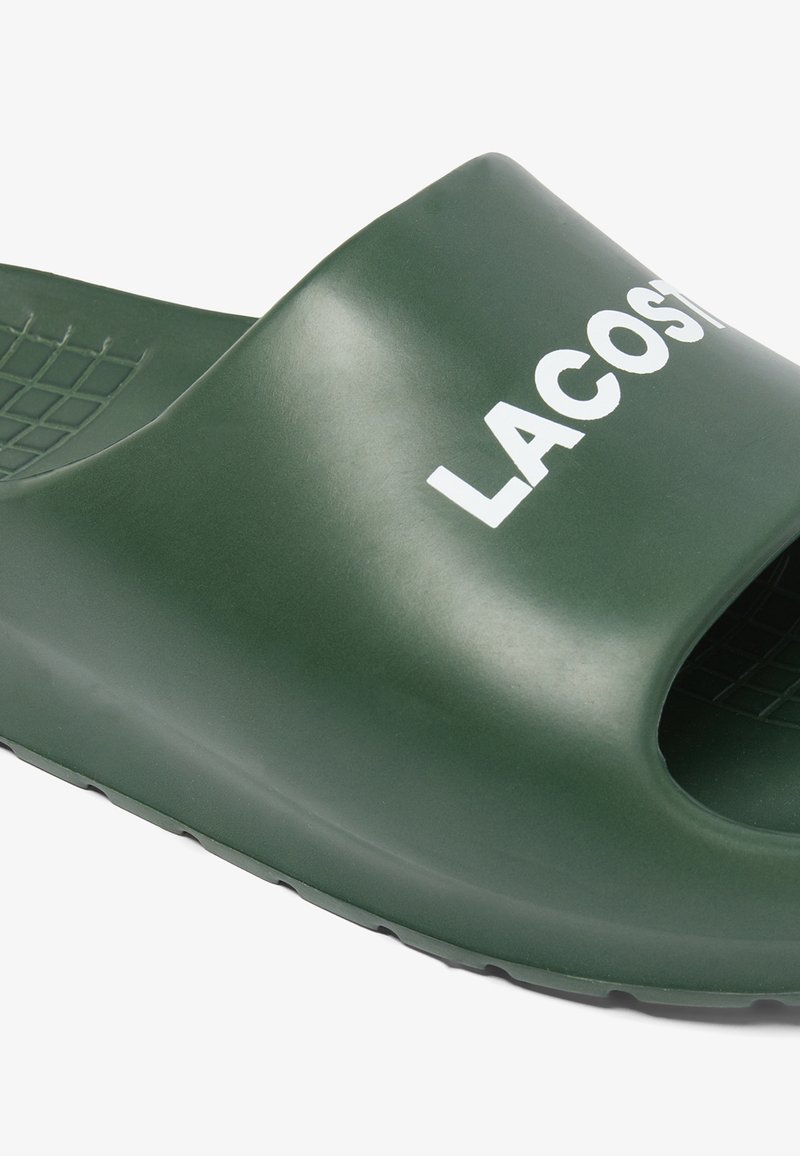 Grüne Gummisandale mit offenem Zehendesign und strukturiertem Fußbett. Mit dem Wort "LACOSTE" in weiß auf dem Obermaterial.