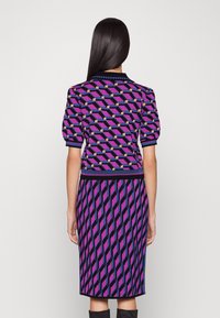 Sukienka dzianinowa z geometrycznym wzorem w kolorach fioletowym, czarnym i pomarańczowym. Krótkie bufiaste rękawy i dopasowana sylwetka, z prążkowanymi akcentami przy dekolcie i u dołu.