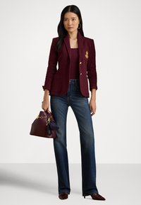 Vīna sarkans žakete ar zelta aksesuāriem, pieguļošs dizains, trīs priekšējie kabatas, kombinēts ar tumši ziliem taisna gada biksēm un saskaņotu somiņu.